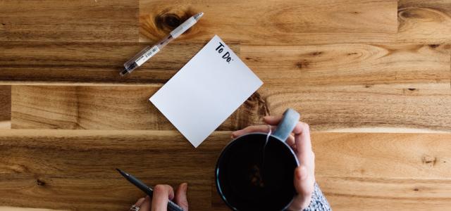 a person writing on a piece of paper next to a cup of coffee by Kelly Sikkema courtesy of Unsplash.